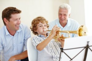 Shot of a cute little boy playing the trumpet while his father and grandfather watch him proudly